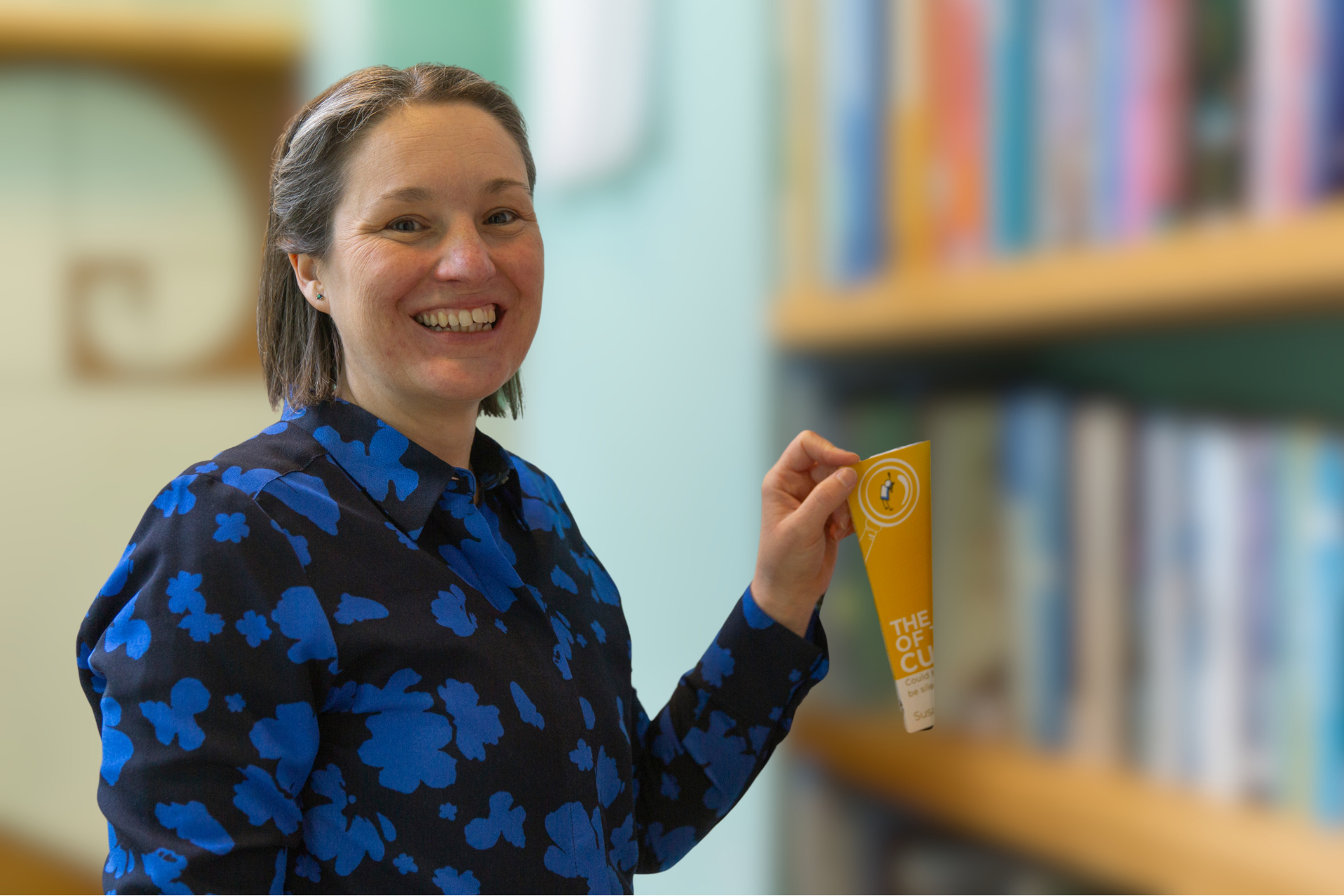 Susannah Simmons smiling as she take her book The Mystery of the Lost Customer off a bookshelf