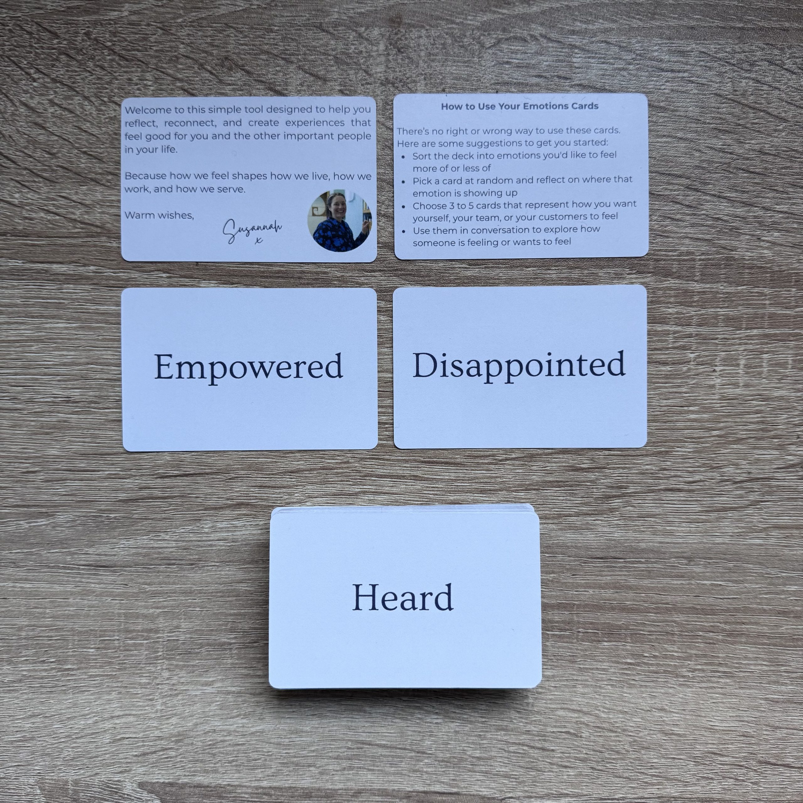 Several Emotions Cards by Susannah Simmons laid out on a wooden surface, including cards that say Empowered, Disappointed, and Heard, along with welcome and instruction cards.